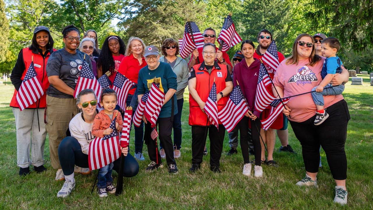 A group of Red Cross volunteers hold small American flags while standing outside.