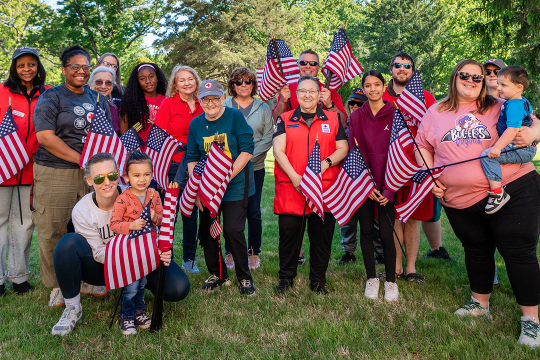 A group of Red Cross volunteers hold flags while standing outside.