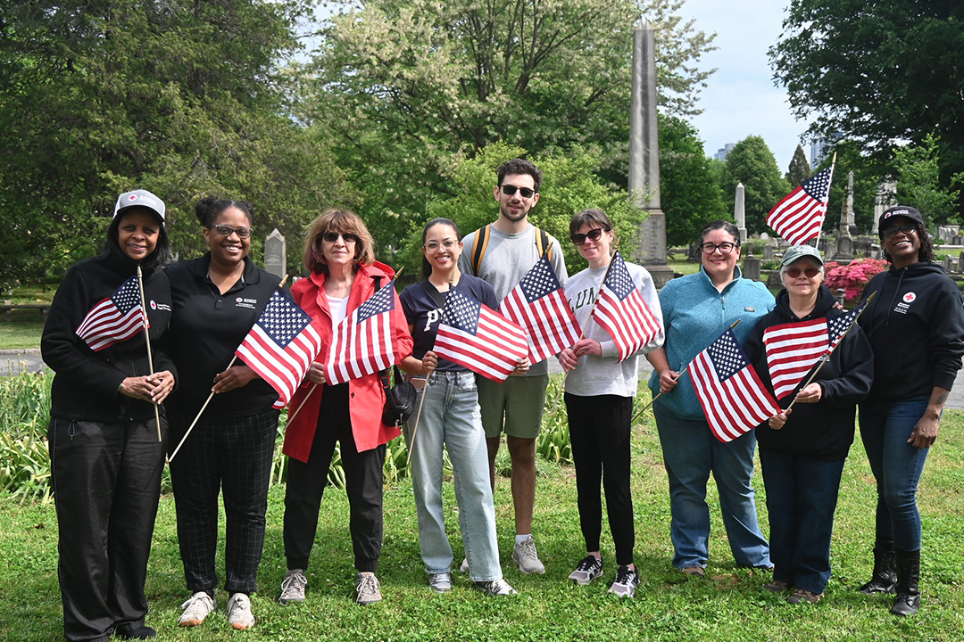 A group of Red Cross volunteers hold American Flags while standing outside.