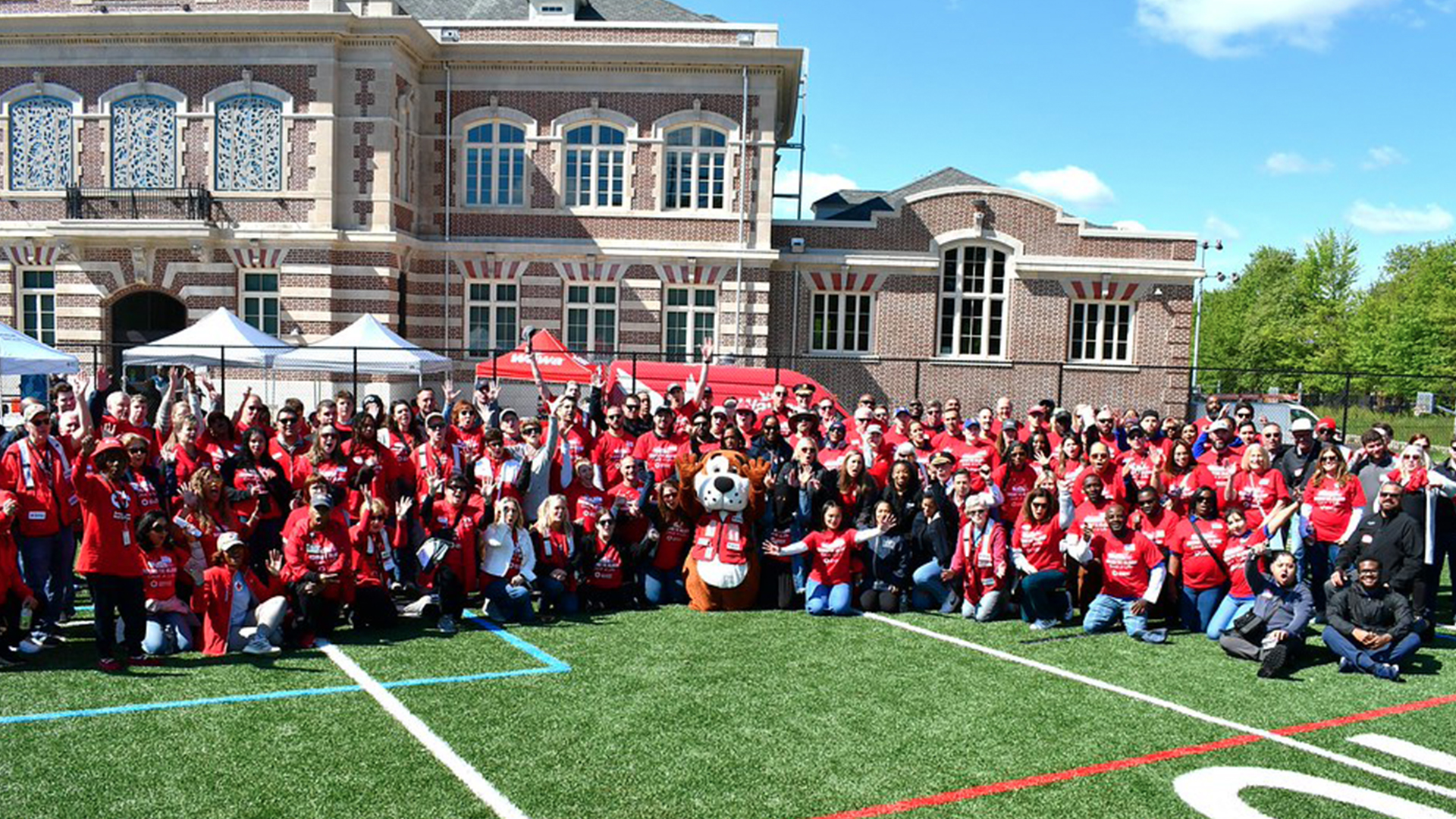 Approximately 200 Red Cross volunteers posing for a group photo on an athletic field wearing red Sound the Alarm T-shirts.