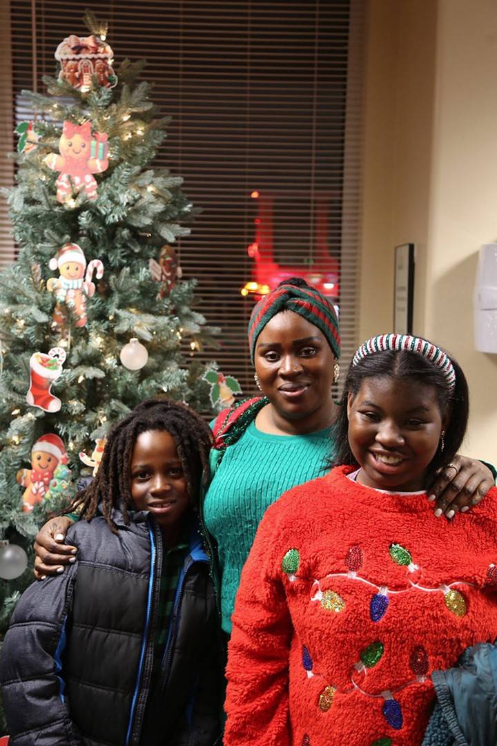 An African American woman stands with a young boy and a teenage girl in front of a decorate Chriistmas tree. 
