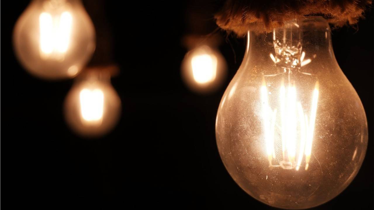 Close-up of several illuminated vintage-style light bulbs hanging against a dark background. One glowing bulb is in sharp focus in the foreground, while three additional bulbs appear softly blurred behind it, creating a warm amber light and emphasizing the concept of electricity, energy, or power.