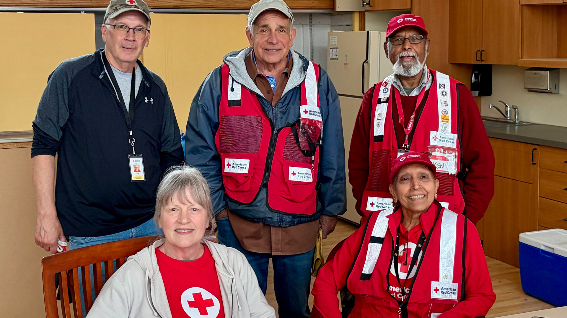 Five American Red Cross volunteers wearing red vests pose for a photo at a shelter.