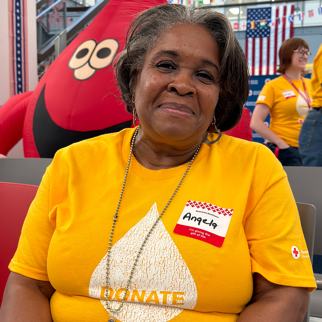 A smiling Red Cross employee in a yellow "DONATE" shirt poses at a blood drive.