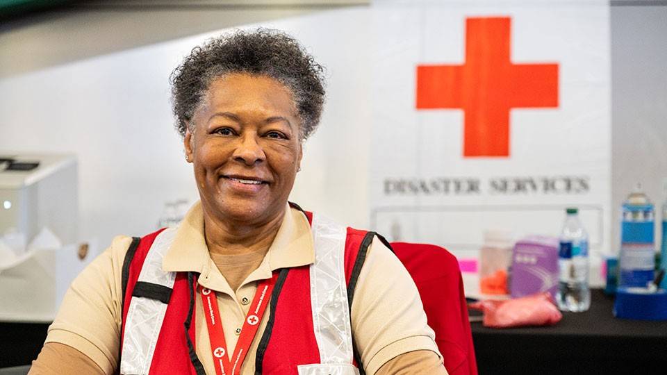 American Red Cross volunteer Brenda Bridges sitting in chair wearing a Red Cross volunteer uniform.
