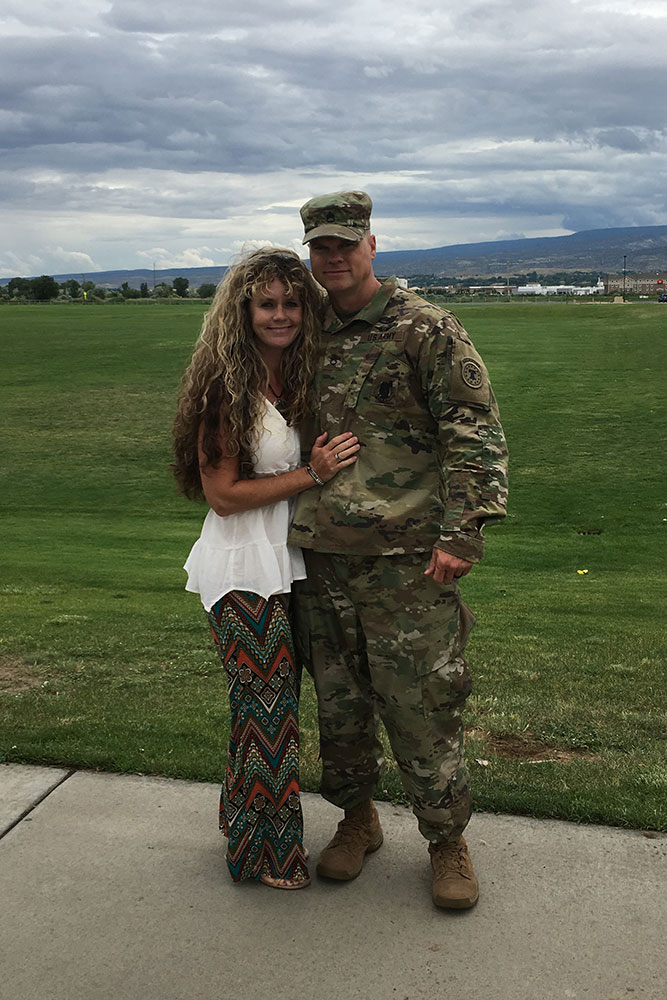 Brandy and her husband, in camouflage military uniform, pose for a photo together.