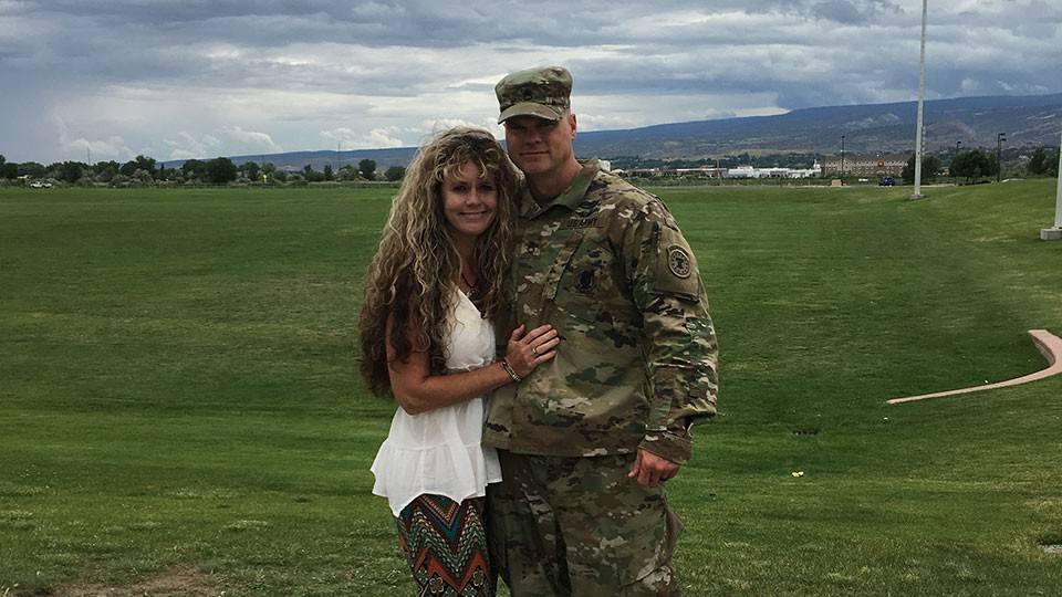 Brandy and her husband, in camouflage military uniform, pose for a photo together.