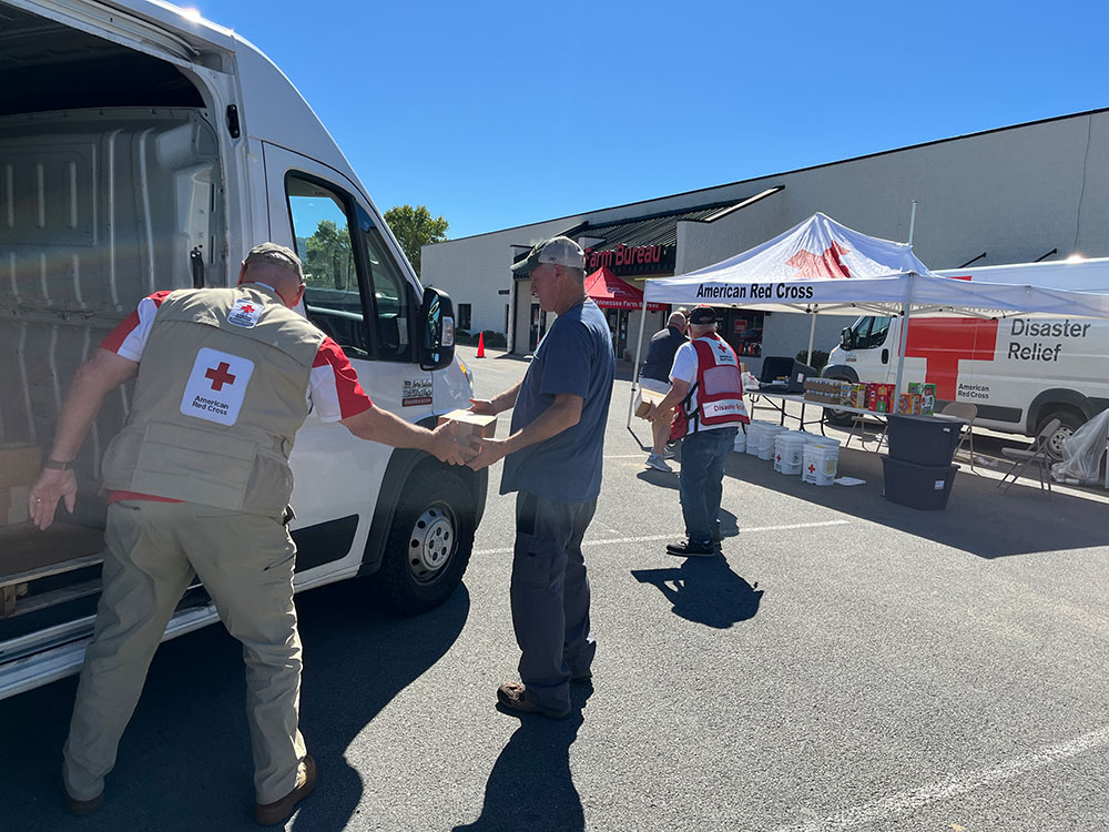 Red Cross volunteers create an assembly line and unload boxes from a van in a parking lot.