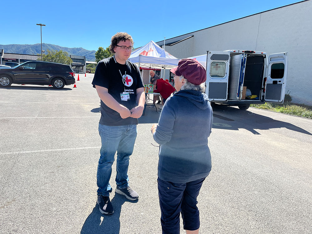 Red Cross volunteer speaking to a person in a parking lot.