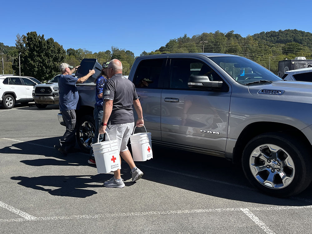 Red Cross volunteers carrying Red Cross 5 gallon buckets and unloading the back of a truck in a parking lot.