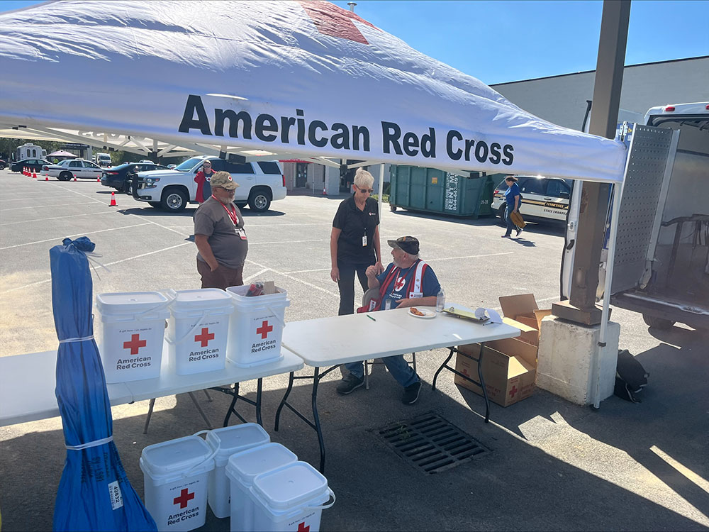 Red Cross volunteers uner a Red Cross canopy with Red Cross 5 gallon buckets on tables.