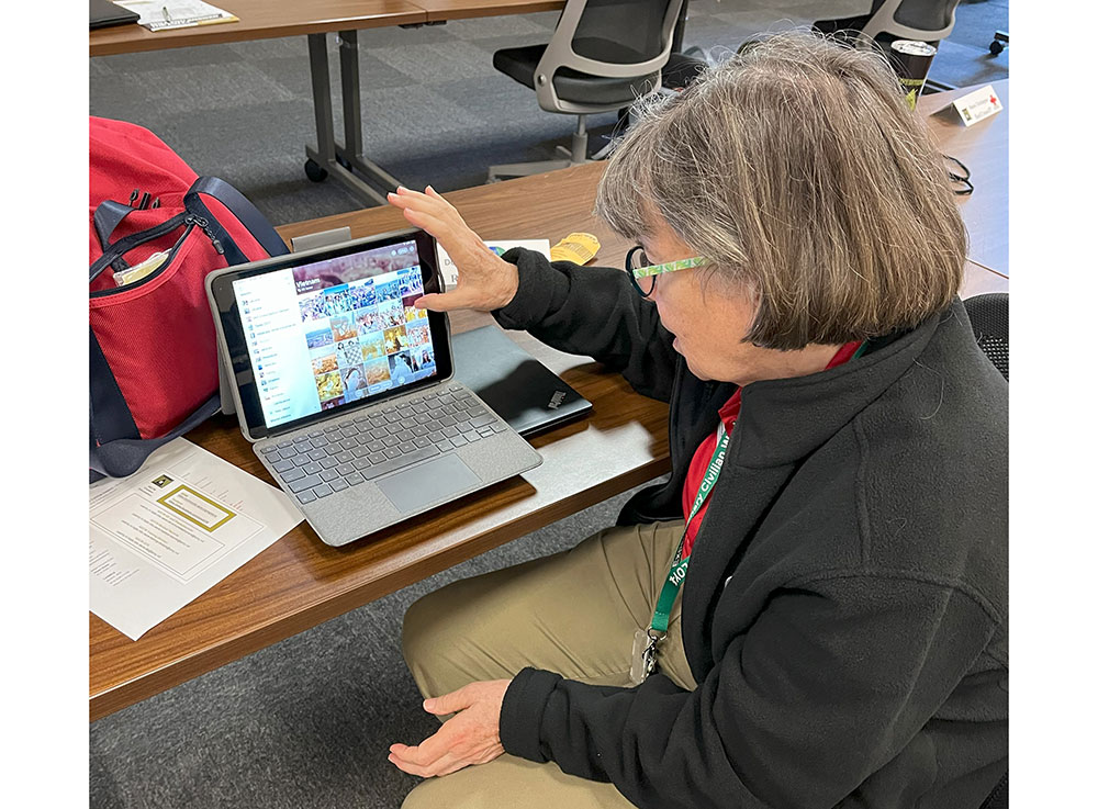 Dorner Carmichael sitting at table with a laptop computer and showing photos from her time volunteering with the American Red Cross in Vietnam.