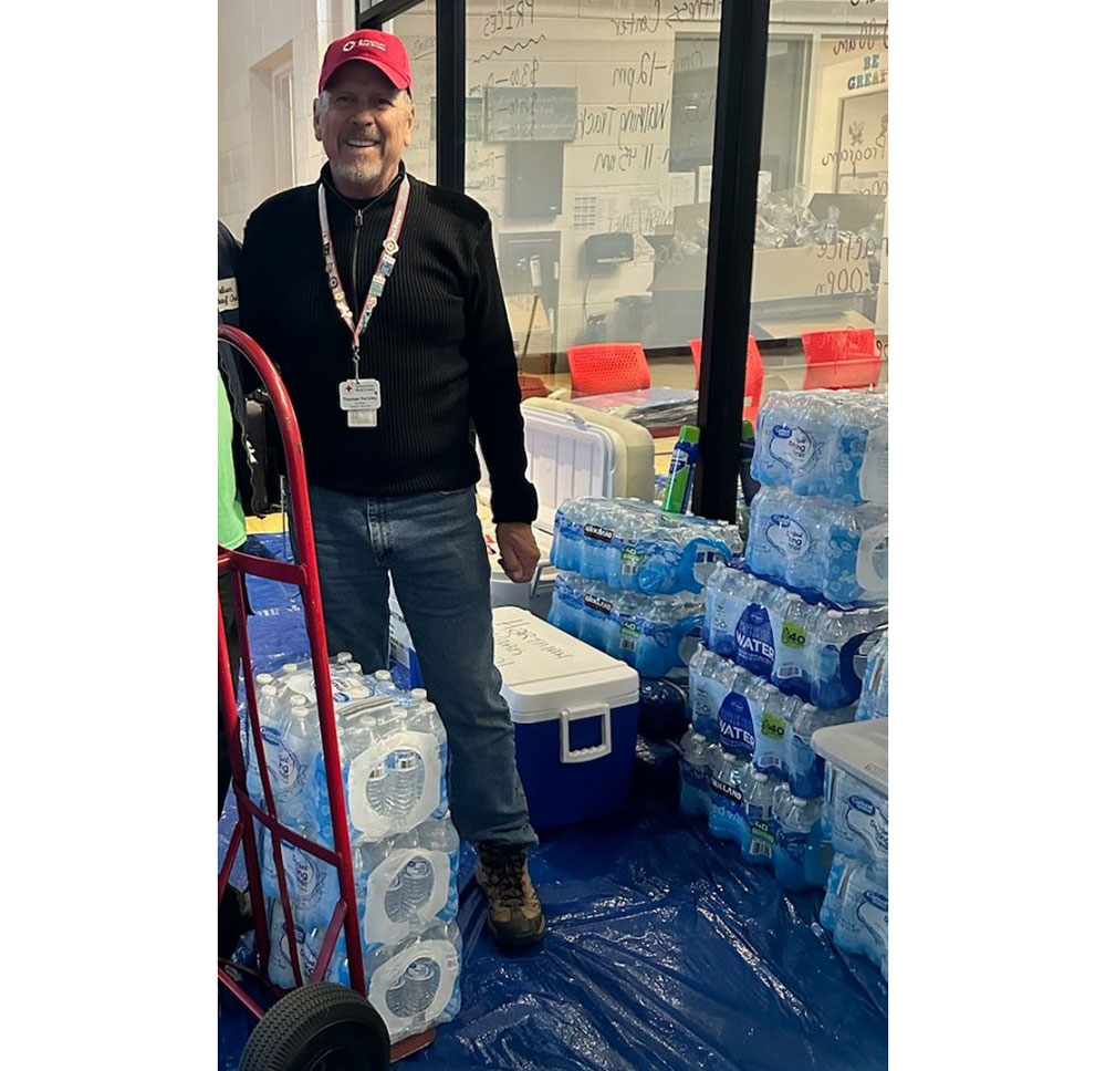 Tom Fortney moving water bottles with a hand cart and wearing an American Red Cross hat and lanyard.