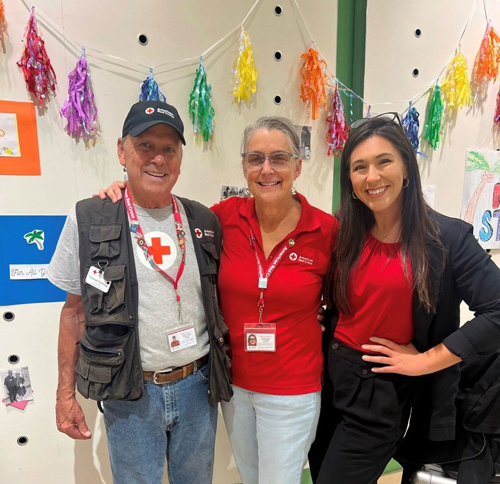 Three America Red Coss volunteers take a group photo next to a wall with decorations.