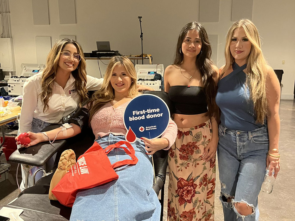 four sisters with one lying in a chair, holding a first-time blood donor sign and donating blood.
