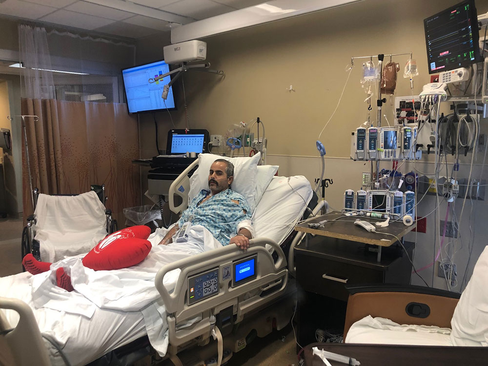 Jose Gonzalez lying in hospital bed with tubes in his nose and bandage on his arm.