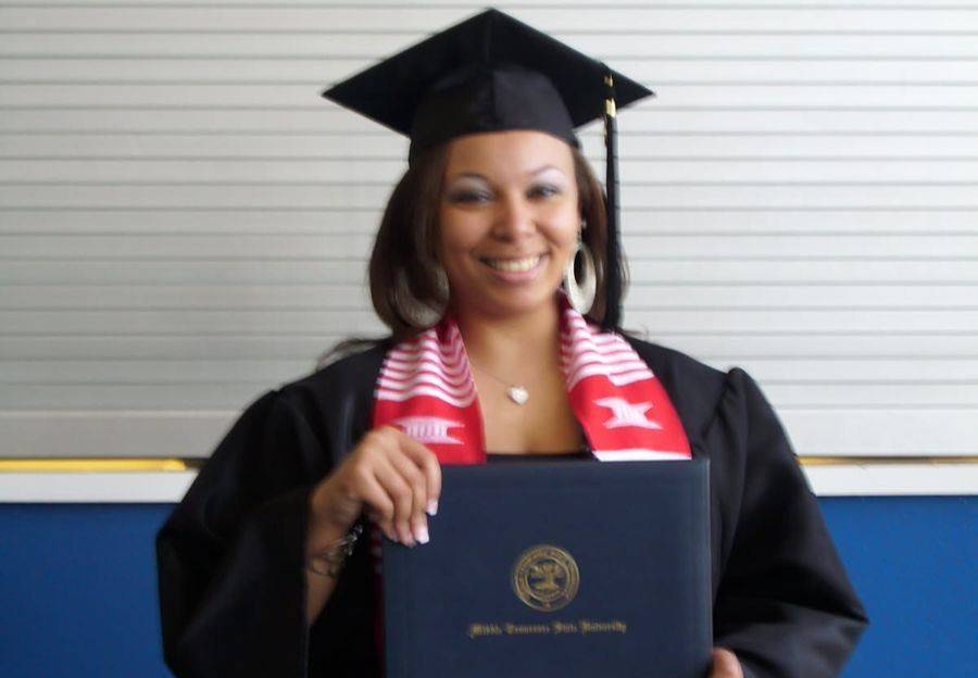 Toya in her cap and gown holding her degree.