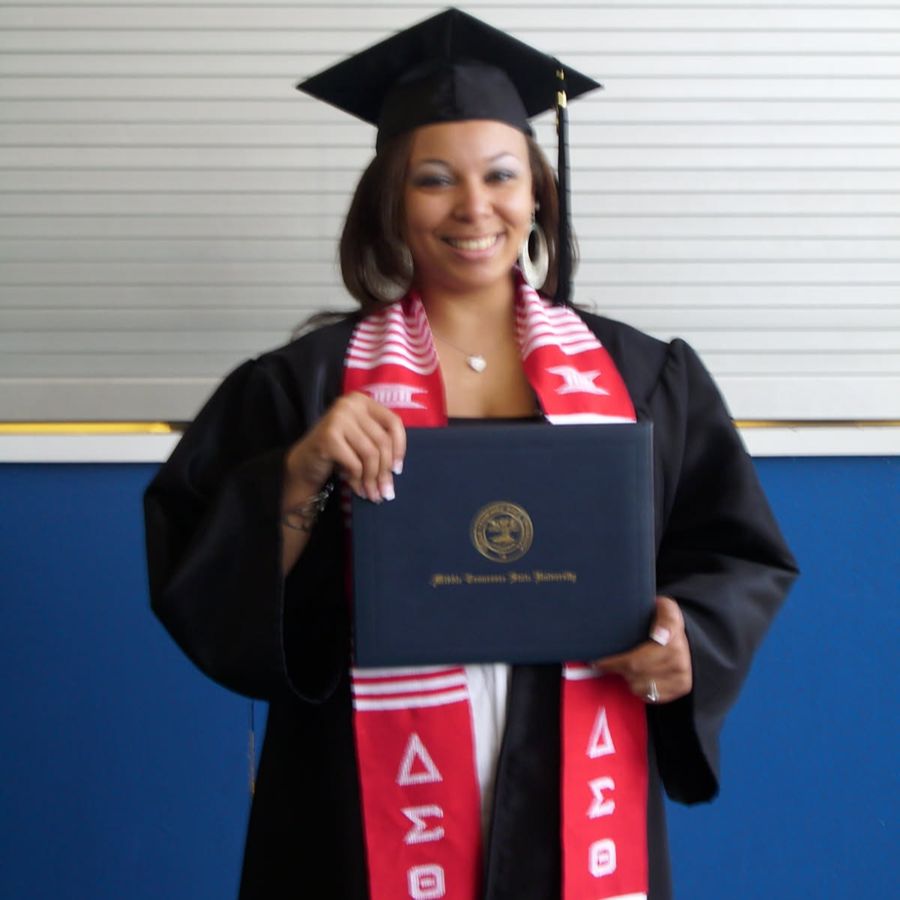 Toya in her cap and gown holding her degree