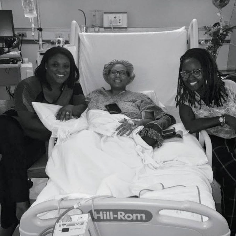 Toay in a hospital bed with two women next to her, holding her hand
