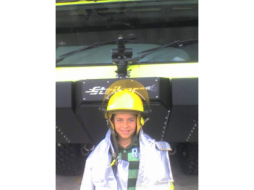 a young Camilo Riviere wearing safety helmet and jacket while standing in front of a large truck.