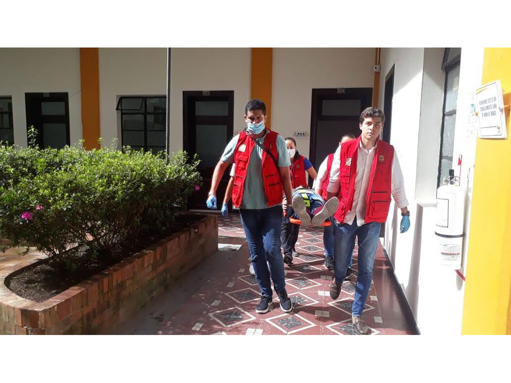 Red Cross volunteers carrying a person on a stretcher in a courtyard.