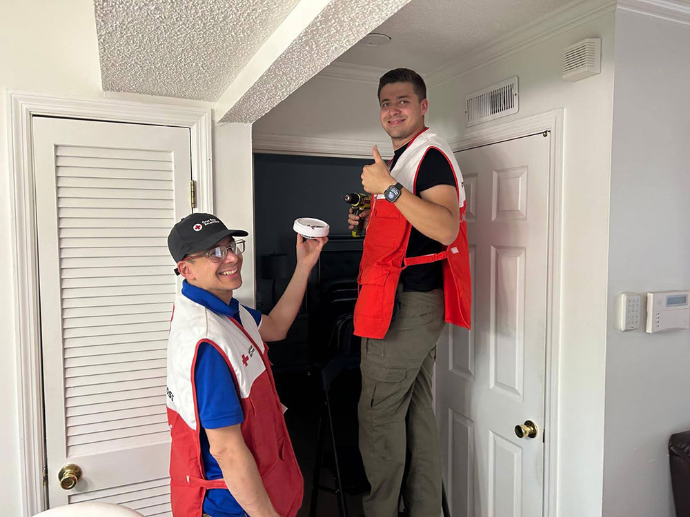 father and son Red Cross volunteers installing a smoke alarm in a home.
