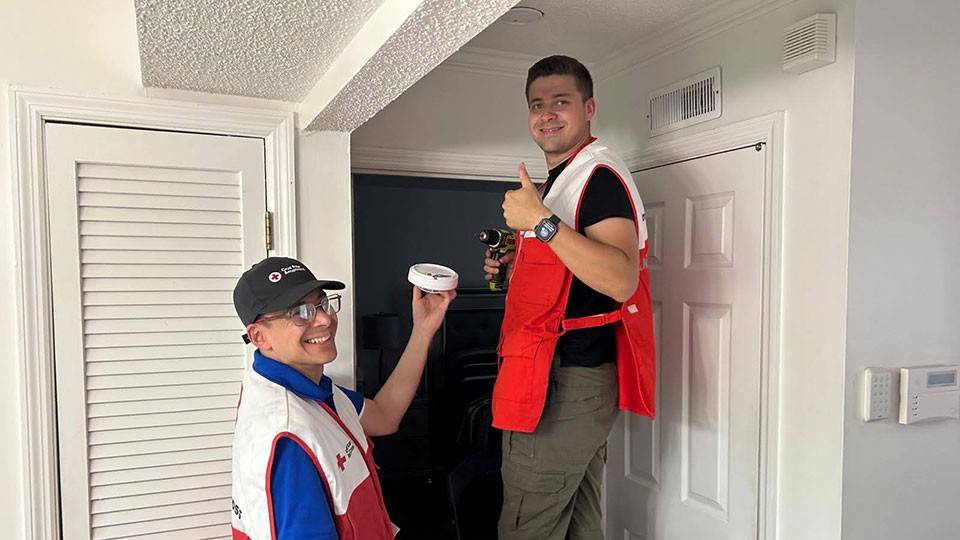 father and son Red Cross volunteers installing a smoke alarm in a home.