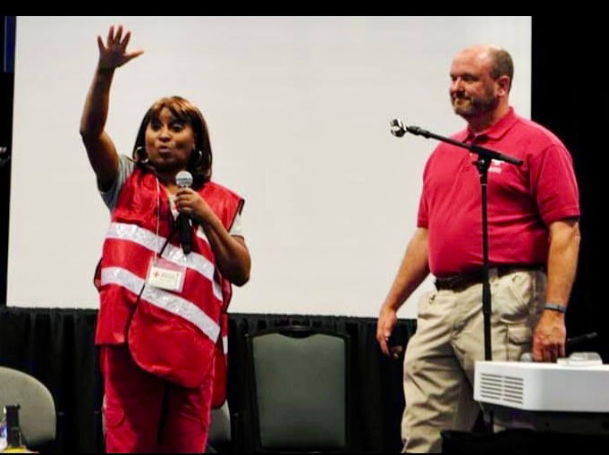 Red Cross volunteer Mary Lockett holding a mic and raising her hand in the air, with another volunteer next to her.