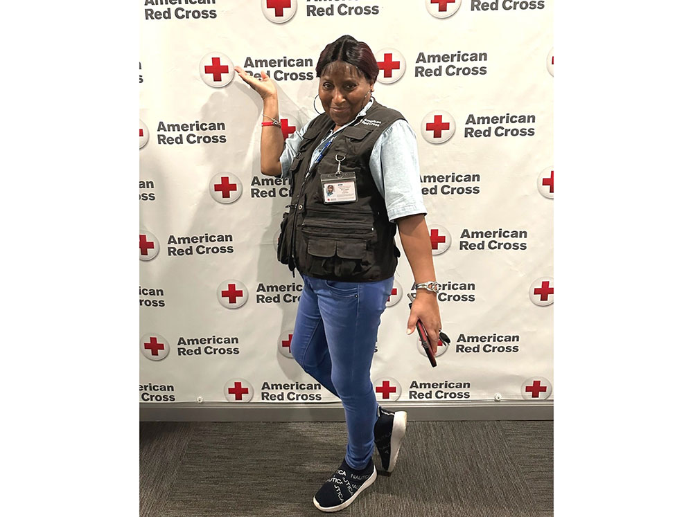 Red Cross volunteer Mary Lockett poses for pic in front of a Red Cross backdrop.