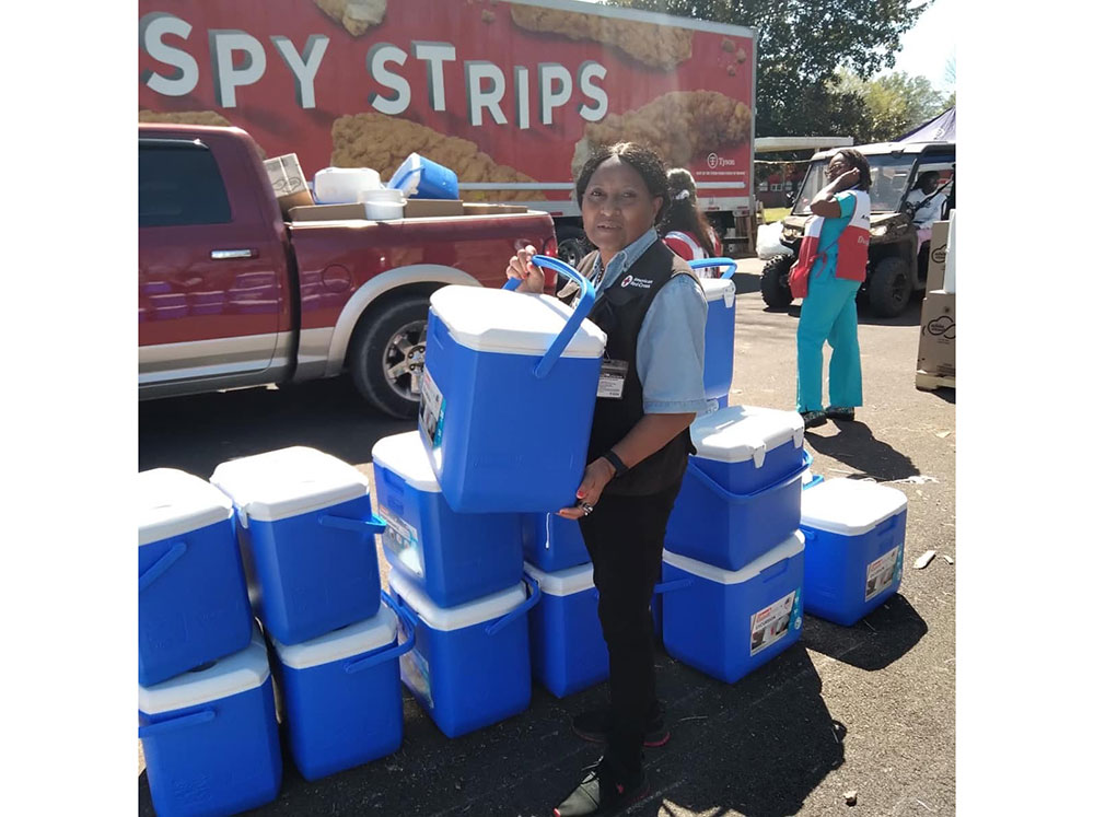 Red Cross volunteer Mary Lockett standing next to a stack of ice chests while holding one in her hands. 