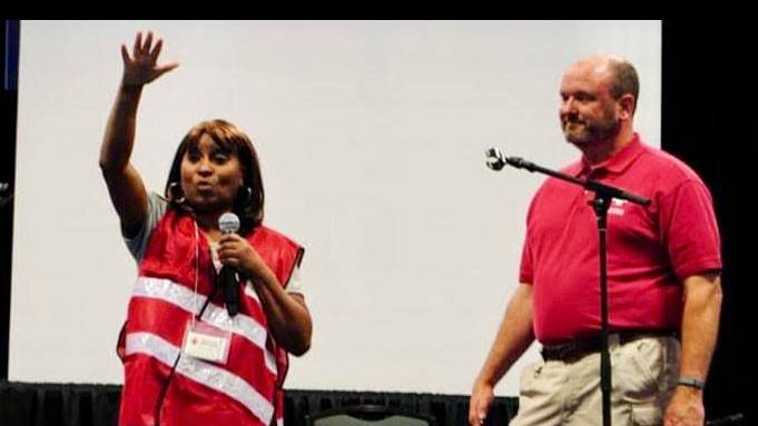Red Cross volunteer Mary Lockett holding a mic and raising her hand in the air, with another volunteer next to her.