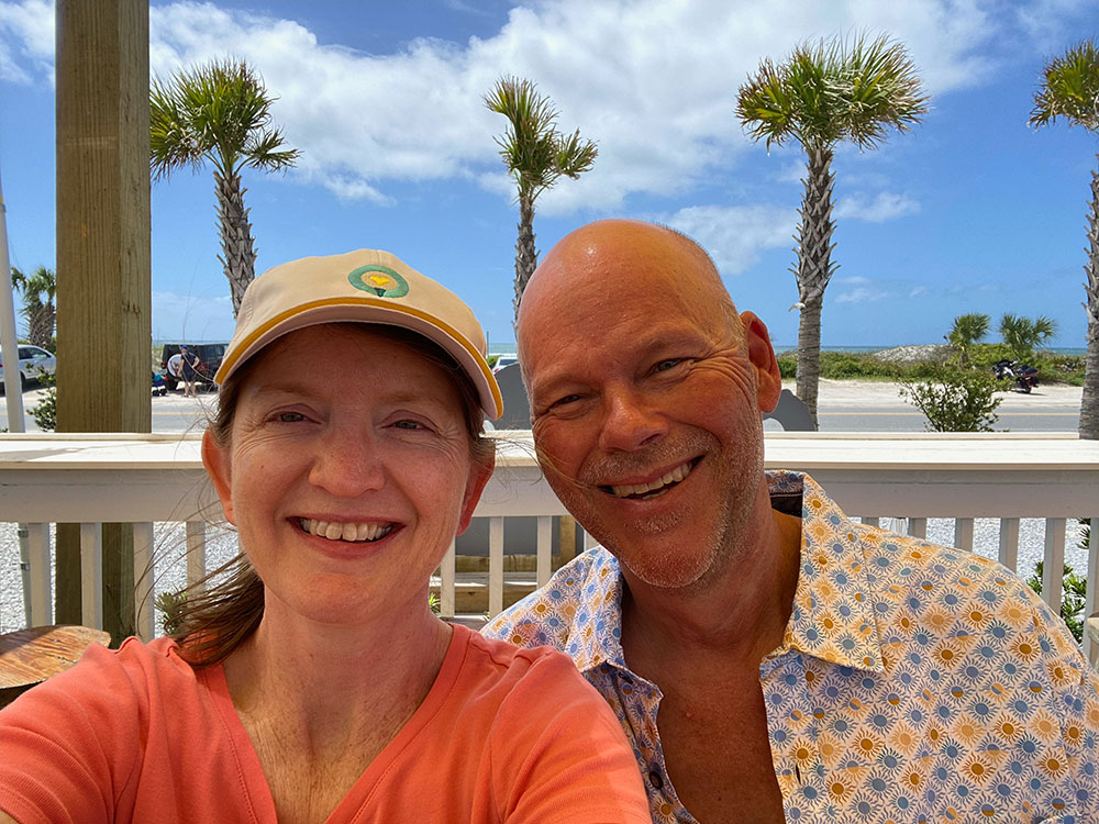 Pete Hinerman and his wife take a selfie outside with palm trees in the background.