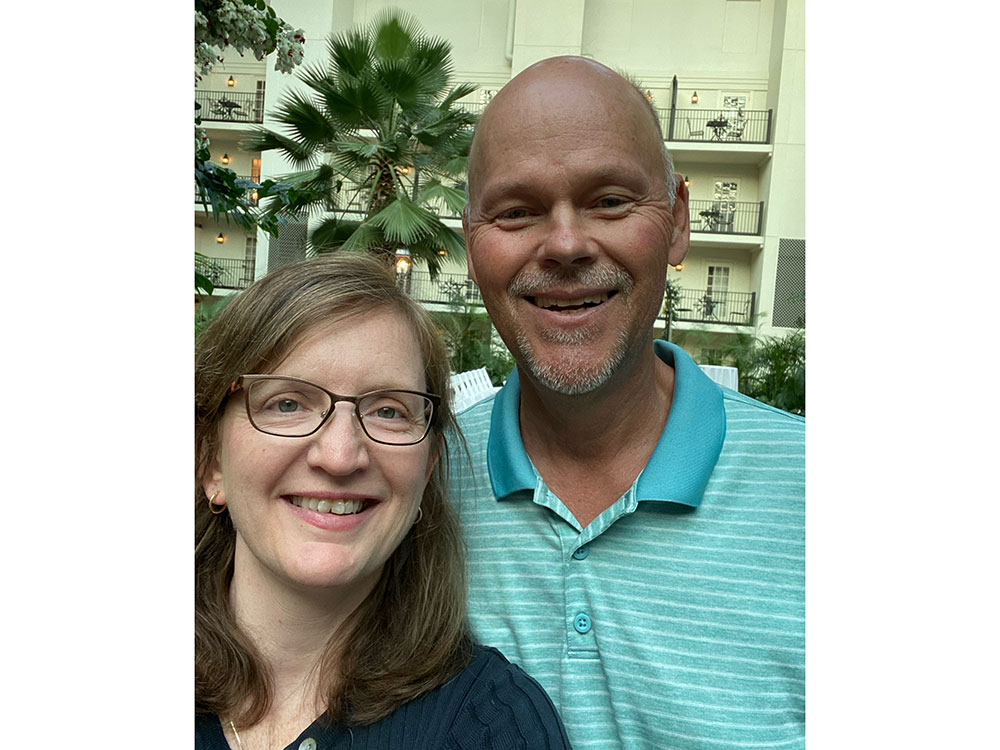 Pete Hinerman and his wife take a selfie outside with palm trees and hotel in the background.