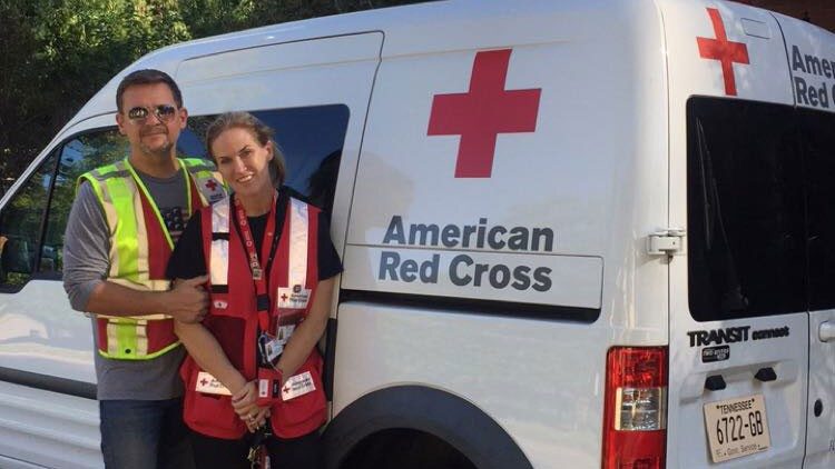 Two Red Cross volunteers standing next to a Red Cross vehicle in front of a house.