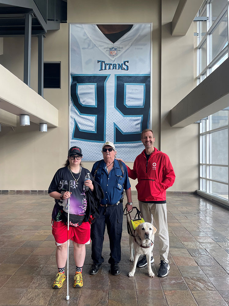 Christel Womack holding a white cane, her father with a seeing eye dog and Red Cross volunteer Ryan Meyer.