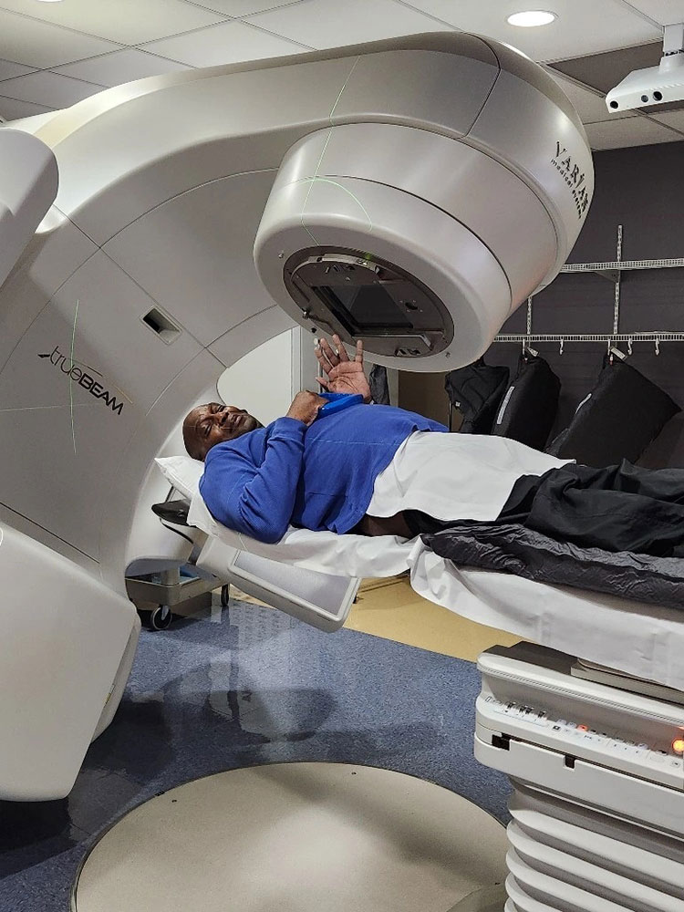 Gary smiles and waves, while lying down, during his last radiation treatment.