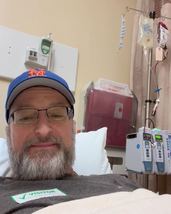 Ralph Campbell with beard, wearing baseball cap and glasses, laying in hospital bed receiving blood at Vanderbilt University Medical Center.