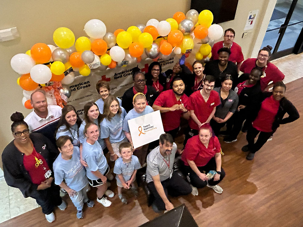 Kaemey Young holding a Team Kaemey sign and a group of blood donors and Red Cross workers with balloons and American Red Cross signs behind them.
