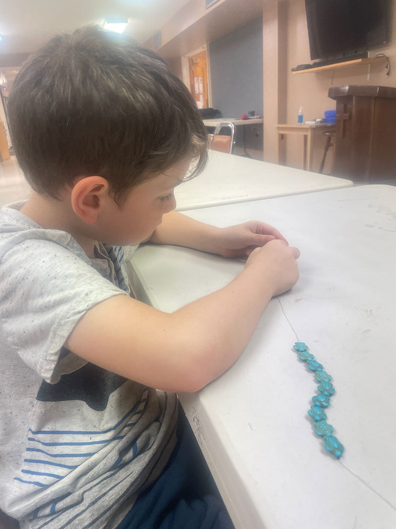 Boy sitting at table reparing his bracelet