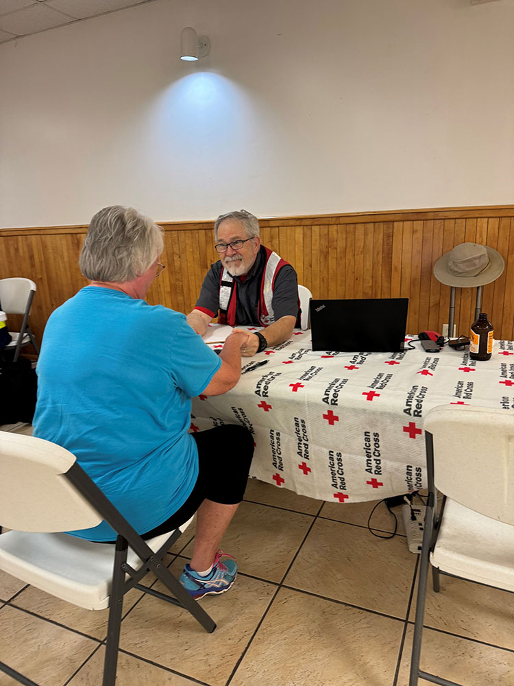 Red Cross volunteer holding hands with person at a table.