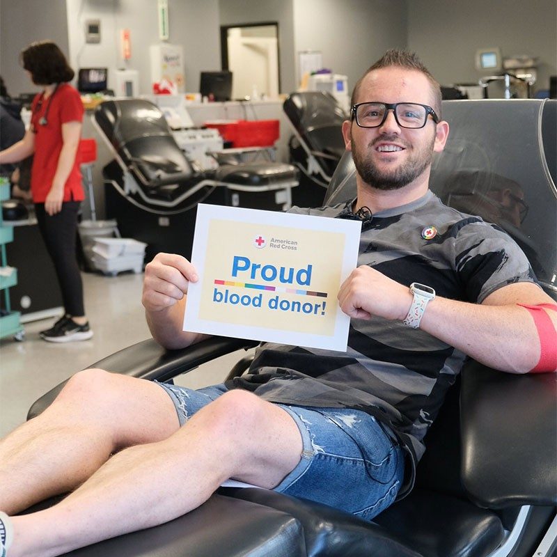 Chris Van Bibber ready to donate blood sitting in cot holding sign