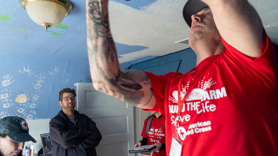 Red Cross volunteer installing a smoke alarm on the ceiling of a home.