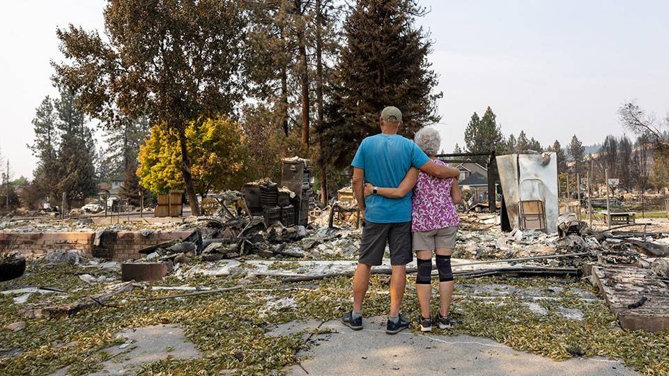 Doug and Georgann Howie, with one arm around each other, while looking at the remains of their burned home.