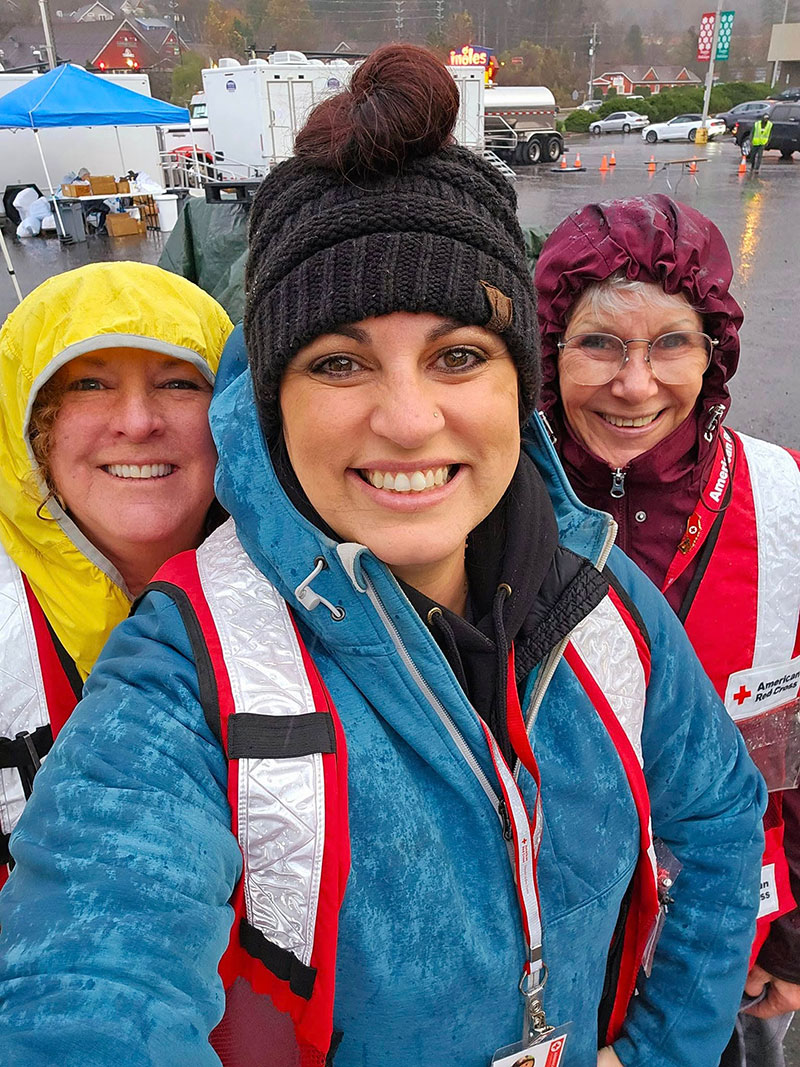 Rachel Rosenbaum wearing headband, sun glasses and Red Cross vest, with two other Red Cross volunteers, takes a selfie.