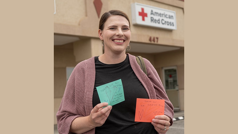 Whitney Klos holding hand written thank you cards in front of a red cross blood donation center.