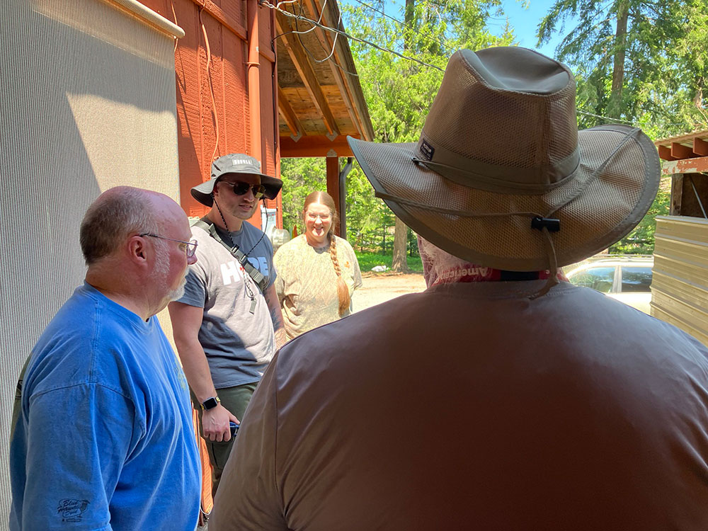 Four people speaking with each other in front of house.