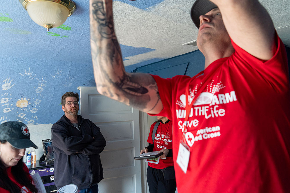 Red Cross volunteer installing a smoke alarm on the ceiling of a home.