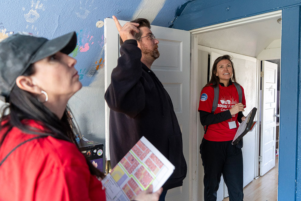 Red Cross volunteers with David Pray inside a room and pointing at the ceiling.