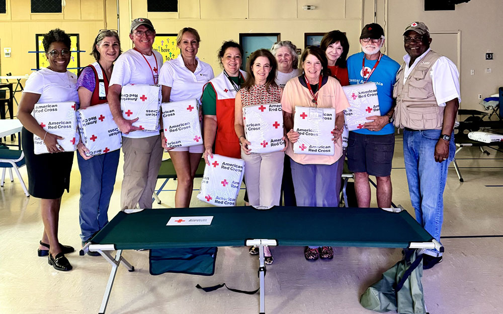 Group pic of Red Cross volunteers in a shelter holding wrapped Red Cross blankets.