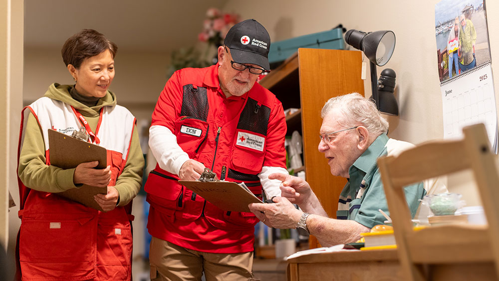 Two Red Cross volunteers showing a retired veteran fire safety info.